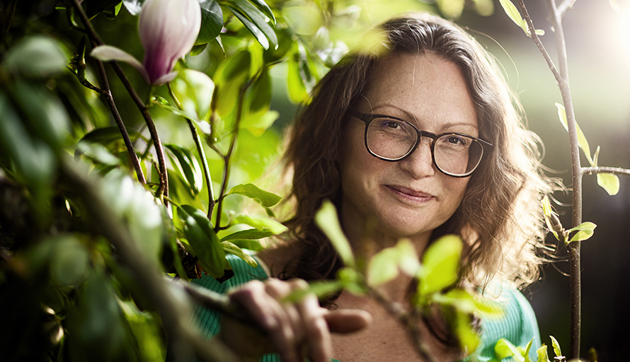 Annie Nellros står i en buske och ler mot kameran, med solljus bakom sig.