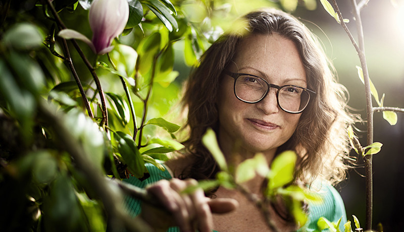 Annie Nellros står i en buske och ler mot kameran, med solljus bakom sig.