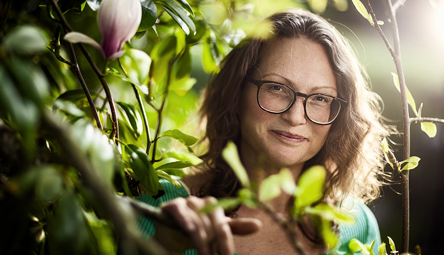 Annie Nellros står i en buske och ler mot kameran, med solljus bakom sig.