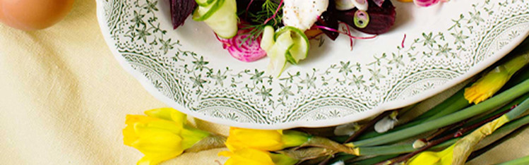 Matjesill, ägg och grönsaker på ett fat. Påskliljor och ägg vid sidan av. Allt på en gul duk.