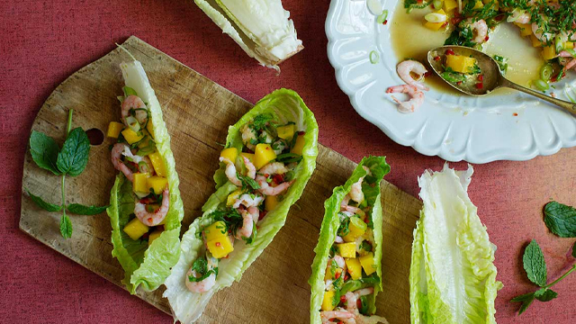 Räksallad med mango i sallatsblad på en skärbräda.