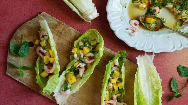 Räksallad med mango i sallatsblad på en skärbräda.