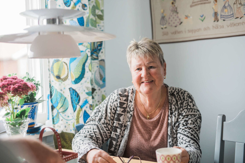 Korthårig kvinna med kaffekopp vid sitt köksbord