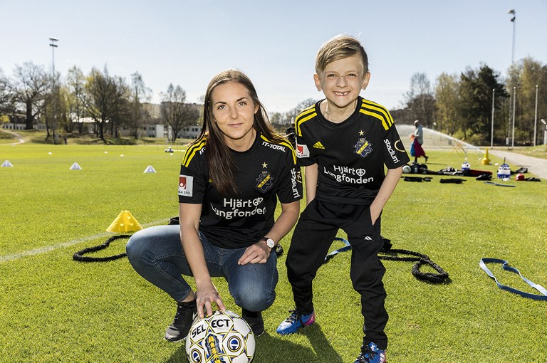 Pojke och kvinna med fotbollströjor från AIK på en fotbollsplan