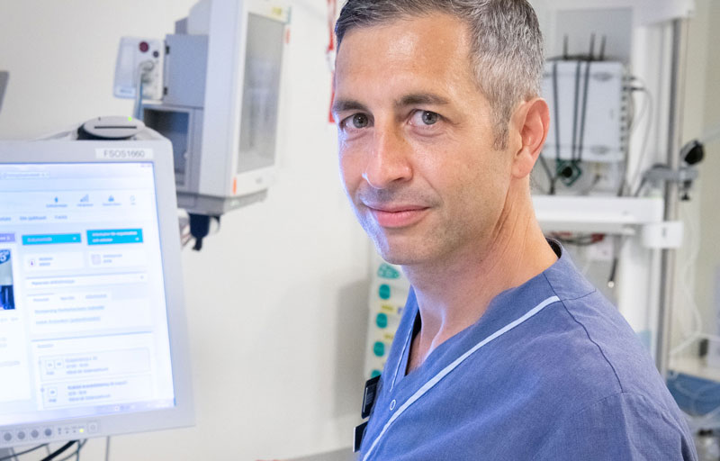 Robin Hofman står vid en datorskärm och tittar in i kameran.