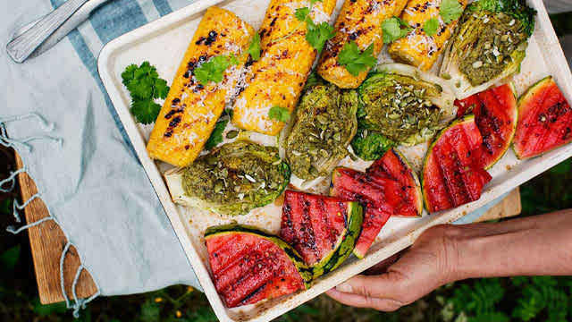 Grillad vattenmelon och majs med mera på en bricka.