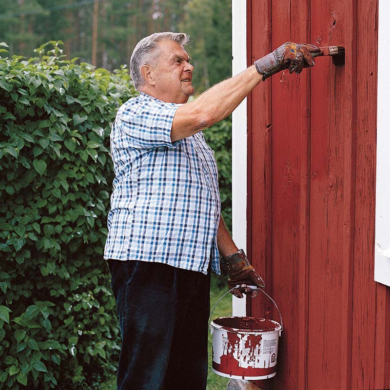 Äldre man målar hus i röd färg