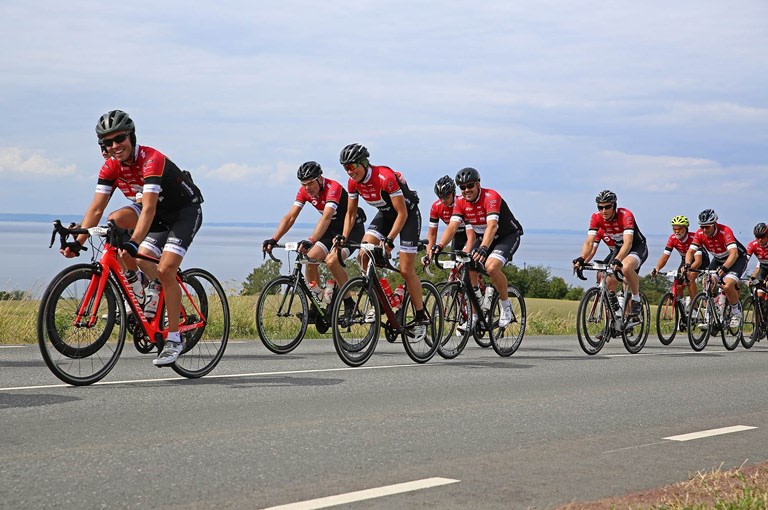Grupp med cyklister i röda tröjor på landsväg