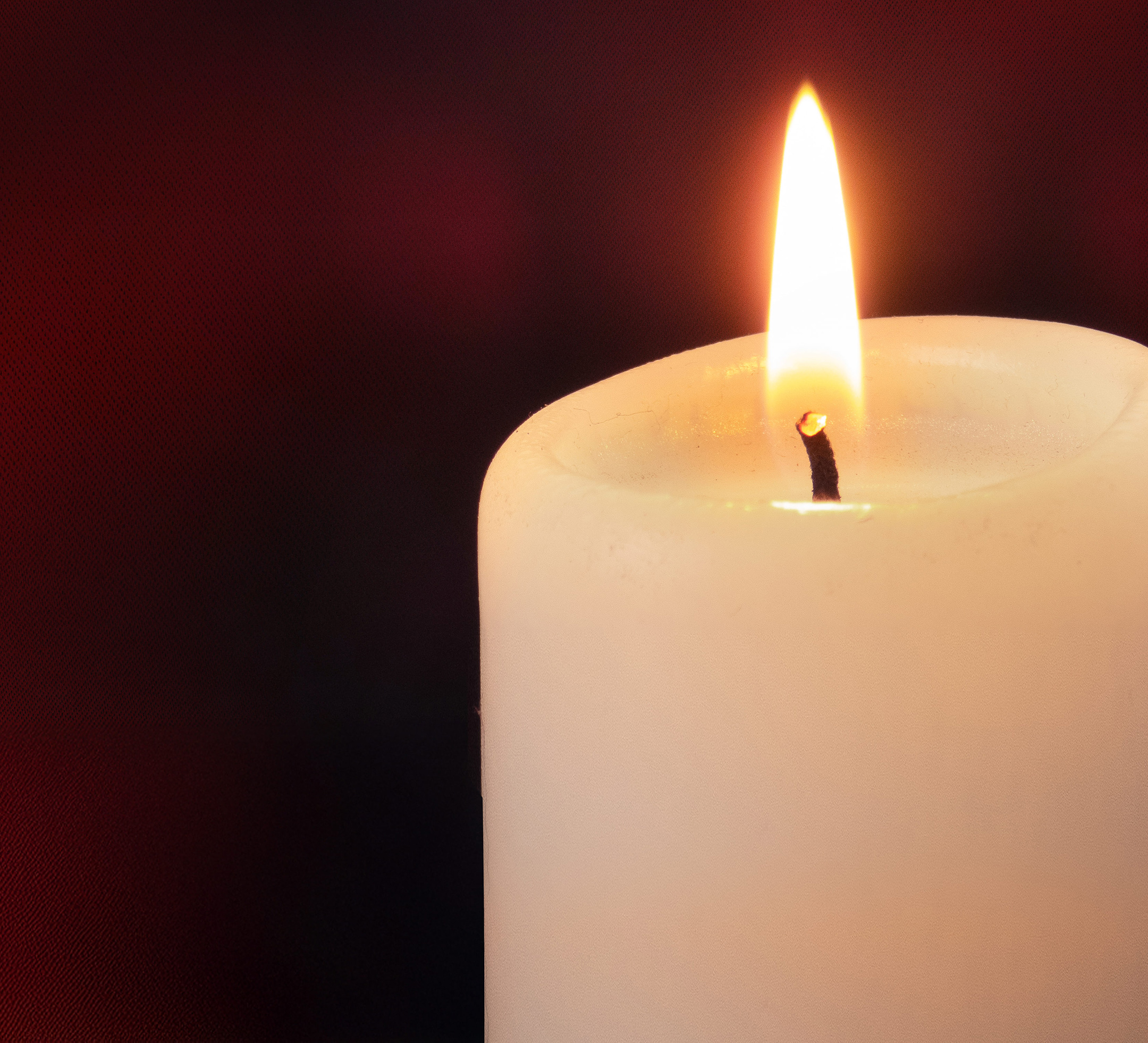 Digitalt minnesljus. Tänt vitt stearinljus mot mörk bakgrund.