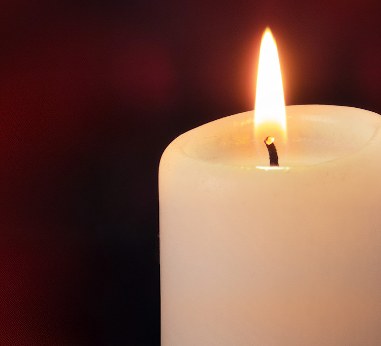 Digitalt minnesljus. Tänt vitt stearinljus mot mörk bakgrund.