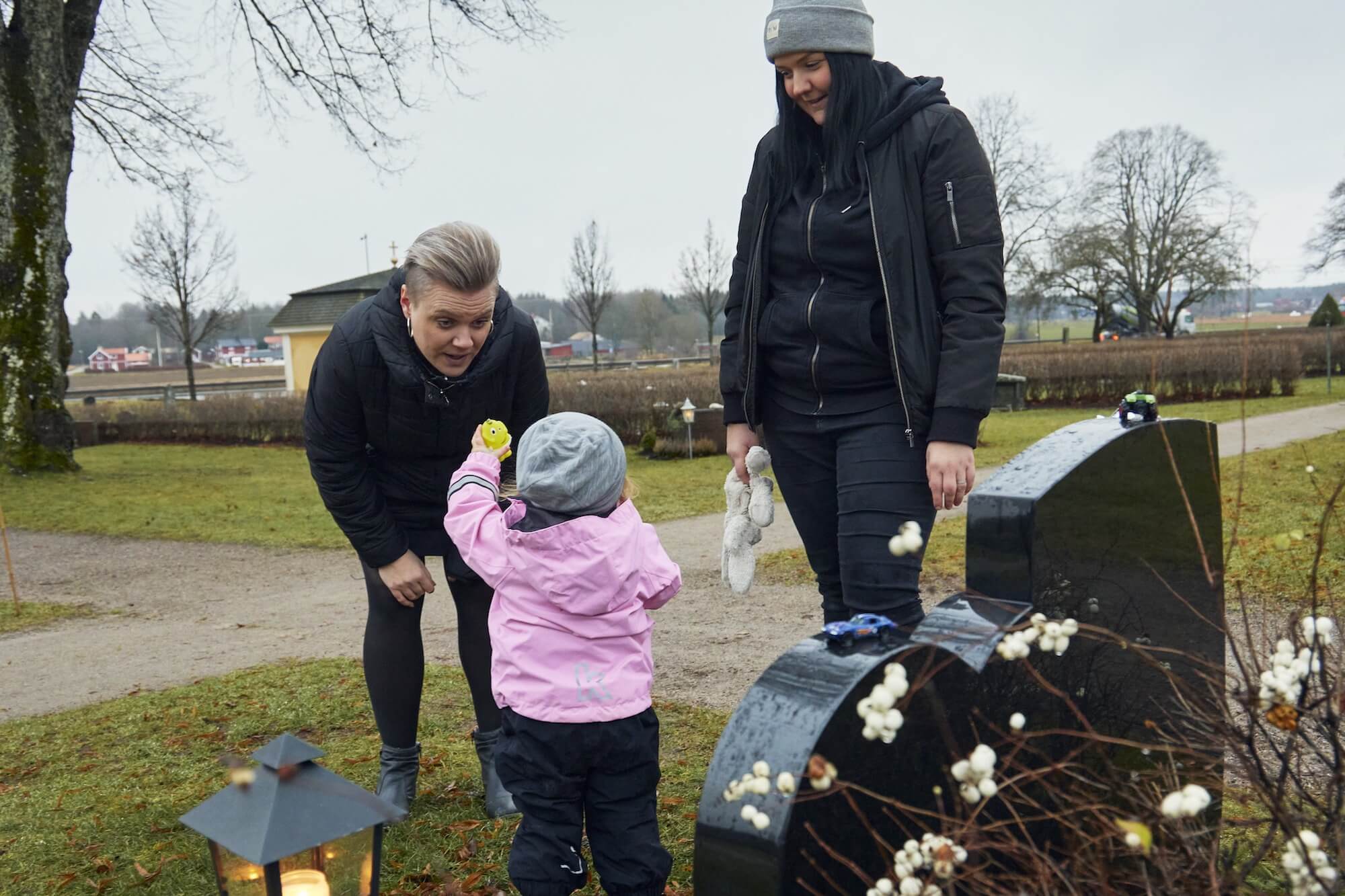 Två kvinnor och ett barn framför grav på kyrkogård