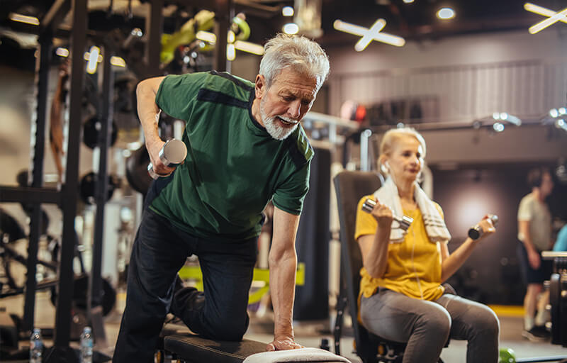 Två personer styrketränar med hantlar på ett gym