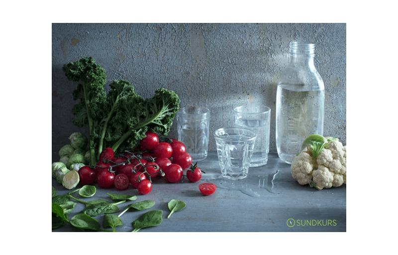 Grönsaker, glas och en flaska med vatten på ett bord
