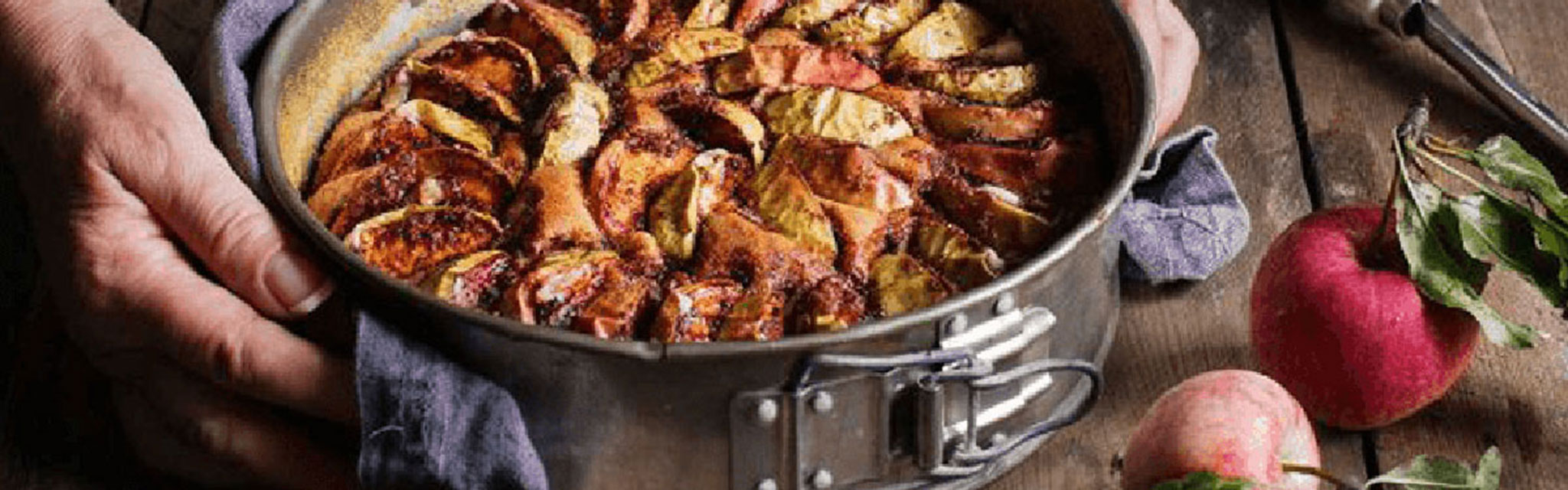 Äppelkaka på ett bord med två äpplen bredvid.