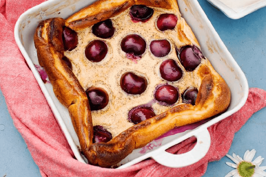 Körsbärsclafouti på ett dukat bord med vita små blommor i höger nederkant.