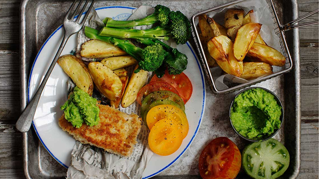 Fish n' chips med tillbehör serverat på en tallrik.