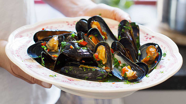 Person håller i en djup skål med kokta blåmusslor.