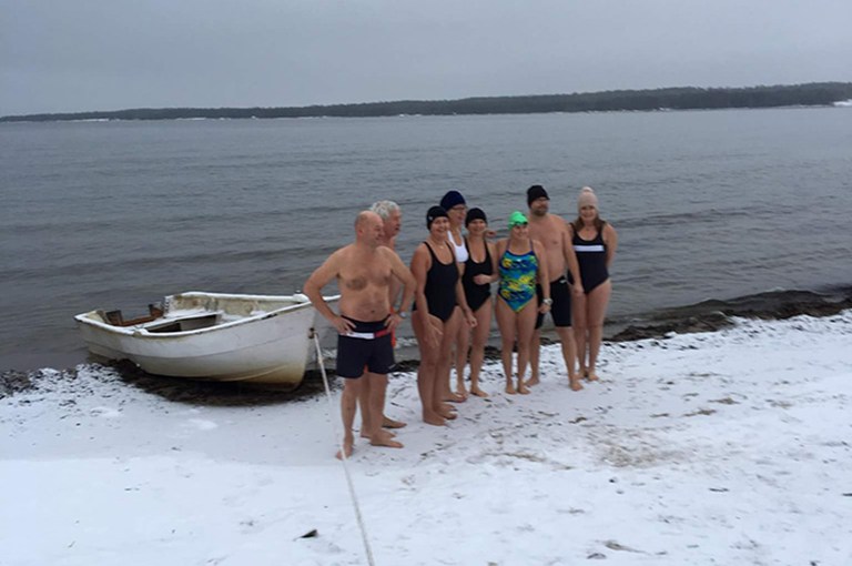 Grupp med vinterbadare på en snötäckt strand