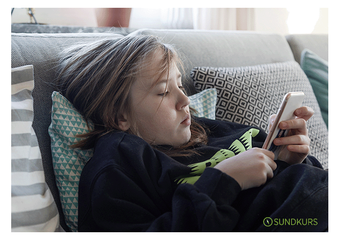 Ett barn ligger i soffan och håller sin mobiltelefon