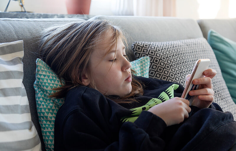 Ett barn ligger i soffan och håller sin mobiltelefon