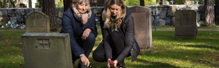 Två kvinnor planterar en blomma vid en grav.