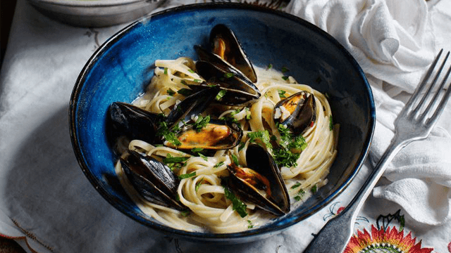 Musselpasta i en tallrik med en gaffel bredvid.