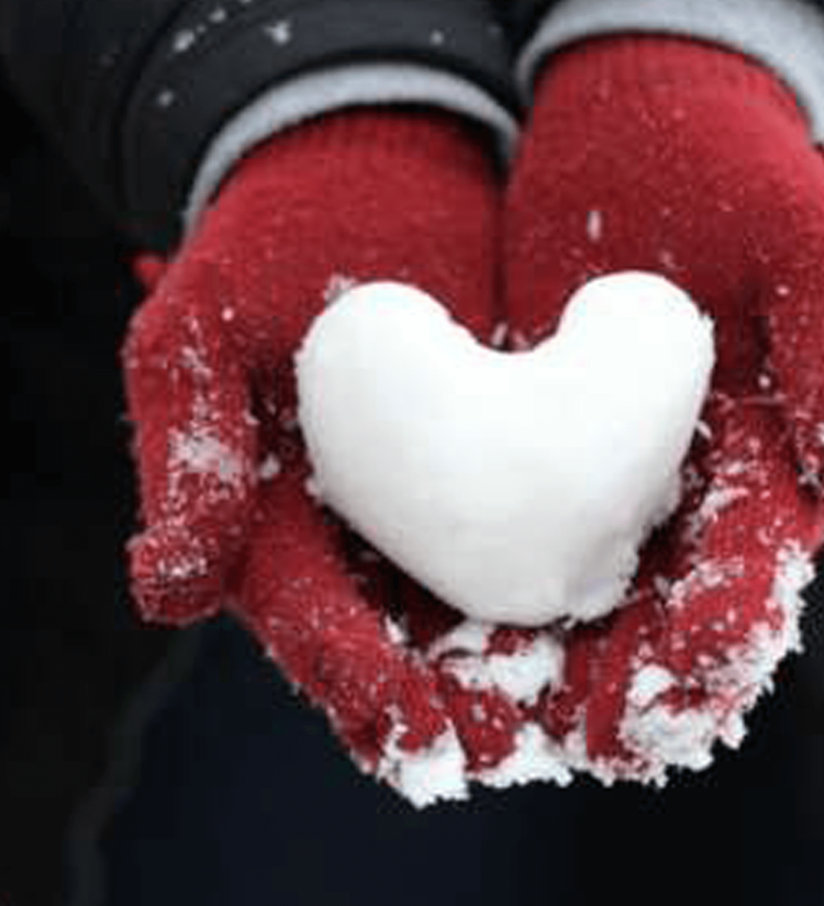 Händer med röda vantar håller ett snöhjärta