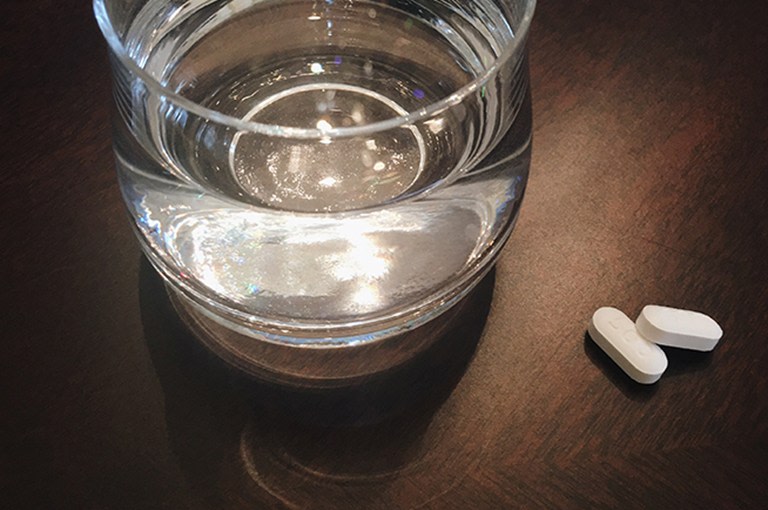 Ett vattenglas med två piller på ett bord