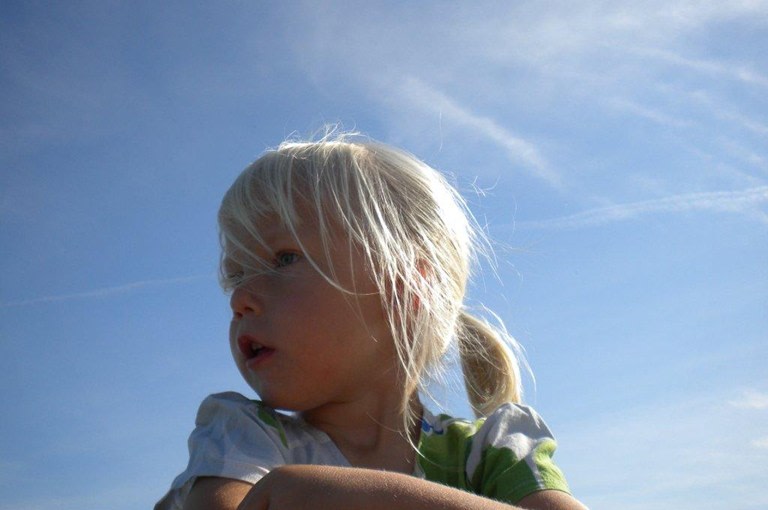 Flicka med blont hår och hästsvans med blå himmel i bakgrunden