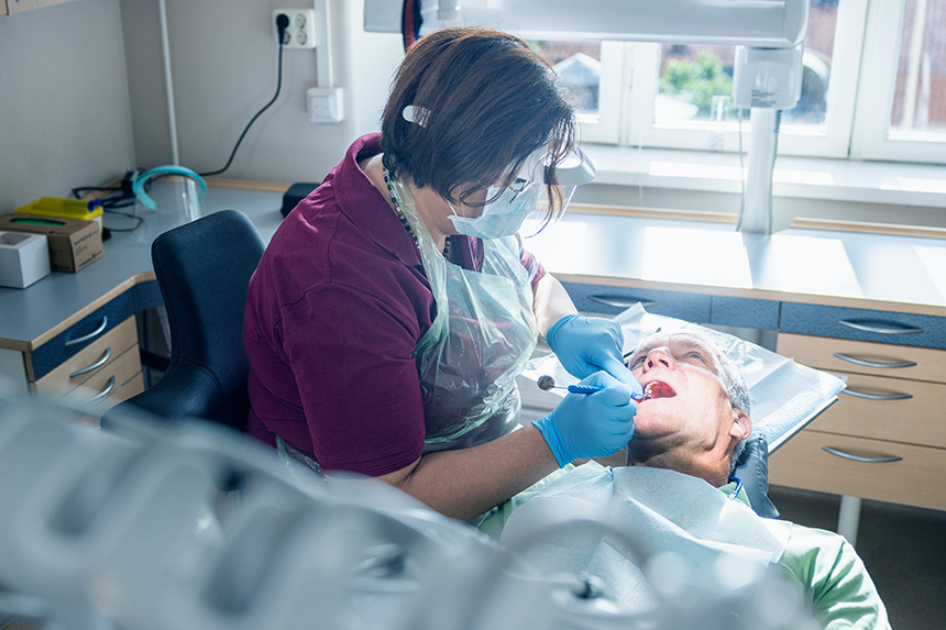 Man i tandläkarstol och tandläkare som utför undersökning
