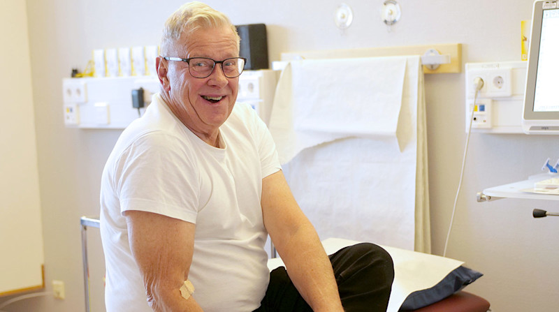 Glad man sitter på sjukhussäng.