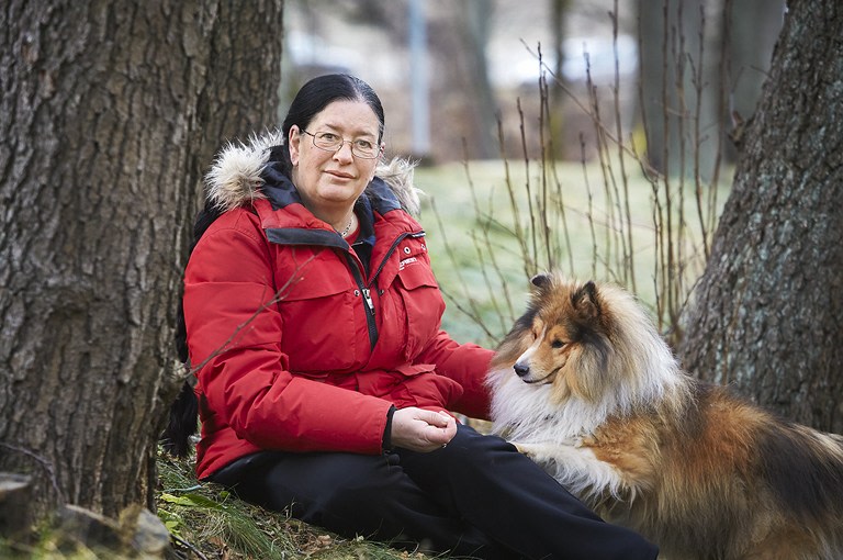 Kvinna med röd jacka och hund sitter vid ett träd
