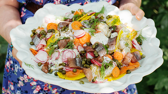 Kvinna håller i en skål med potatissallad med sill och äppeldressing.