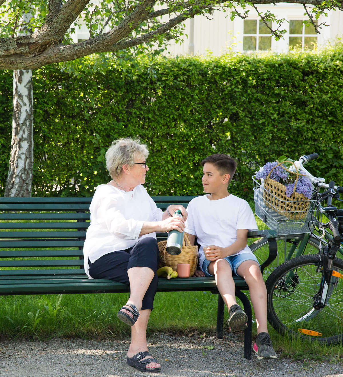 Äldre kvinna och pojke sitter på en parkbänk i somrig park