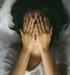En person ligger i en säng med händerna för ansiktet