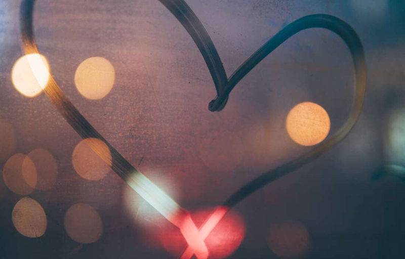 Hjärta ritat på immigt fönster med suddiga ljus i bakgrunden.