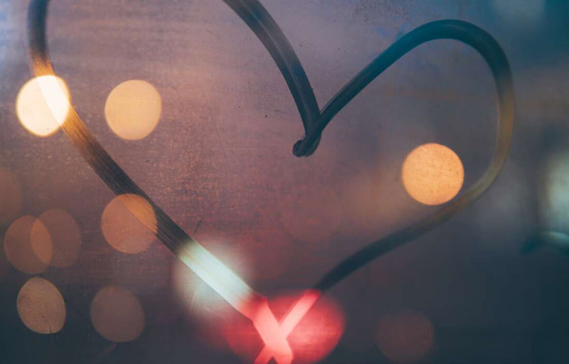 Hjärta ritat på immigt fönster med suddiga ljus i bakgrunden.