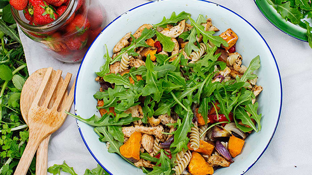 Picknicksallad med sötpotatis, pasta och kyckling uppdukad på ett bord