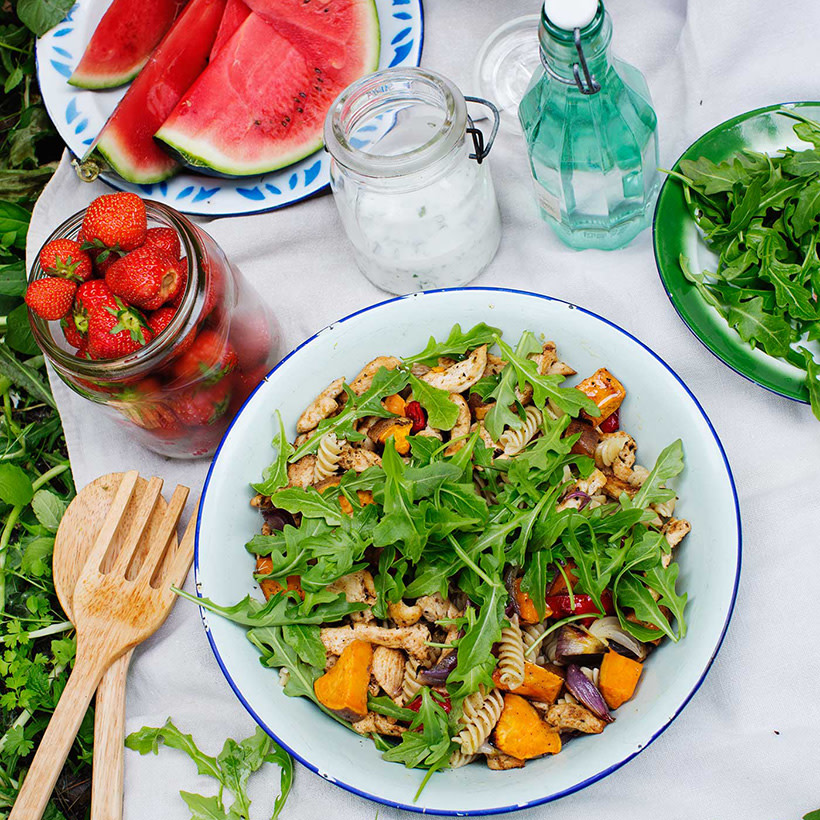 Picknicksallad med sötpotatis, pasta och kyckling på ett uppdukat bord