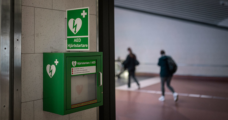 Hjärtstartare på en stenvägg med två människor i förbifarten.