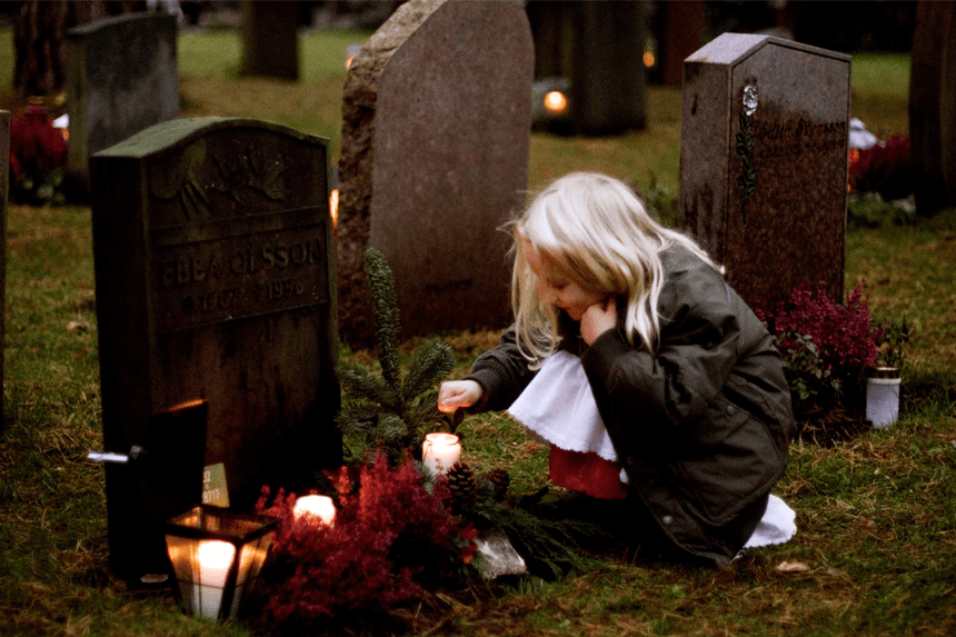 Liten flicka tänder ljus vid en gravplats