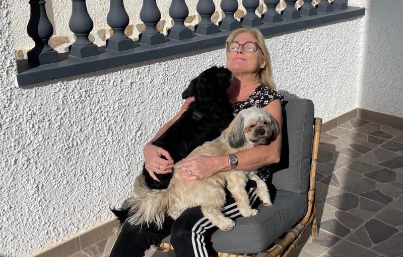 Susanne Wengdell i solen på balkongen med sina två hundar.