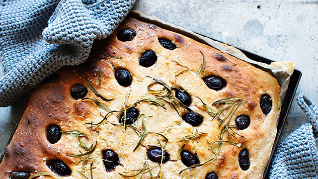 Focaccia med oliver och rosmarin på en plåt.