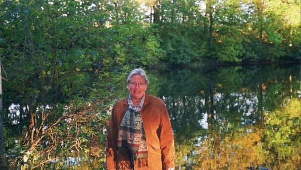 Kvinna i brun jacka vid en skogssjö