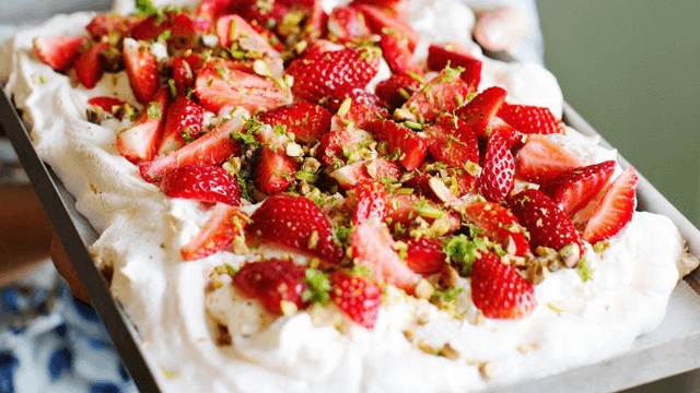 Pavlova-tårta med jordgubbar och hackade pistagenötter ovanpå.