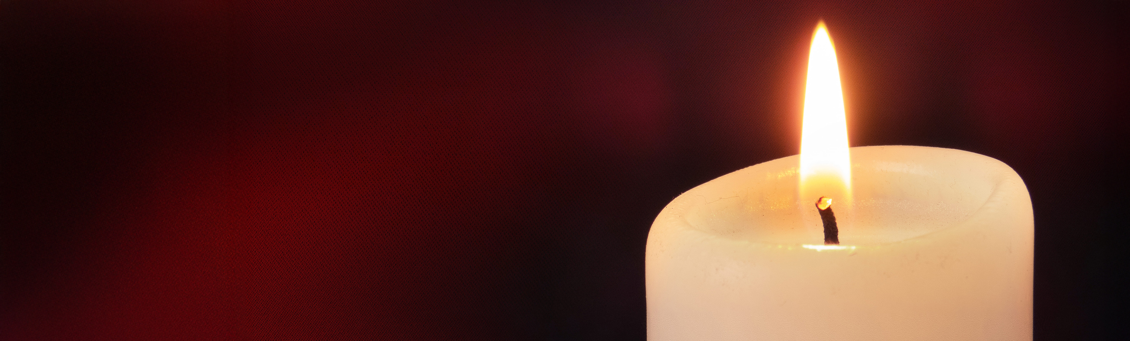 Digitalt minnesljus. Tänt vitt stearinljus mot mörk bakgrund.