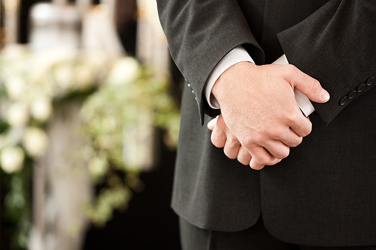 Inzoomning på en mans händer, begravning i bakgrunden.