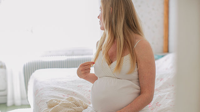 Gravid kvinna i vit klänning som tittar bort från kameran.
