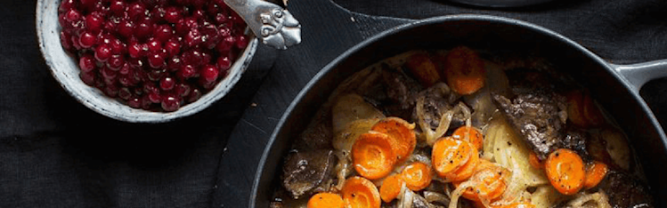 Sjömansbiff i en gryta på ett bord med svart duk. Lingon bredvid i en skål.