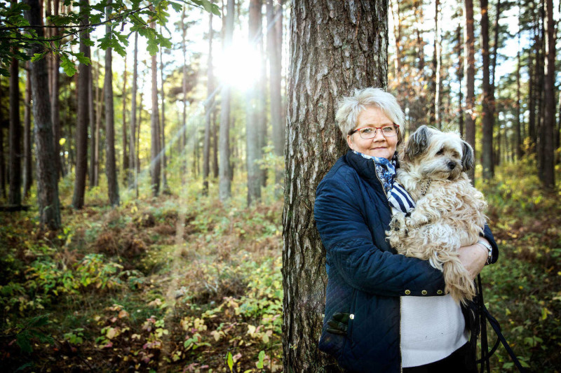 Kvinna i skogsmiljö med hund i famnen